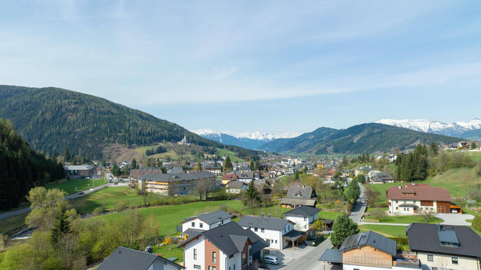 Panoramablick auf eine malerische Berglandschaft mit Siedlung und grünen Hügeln.