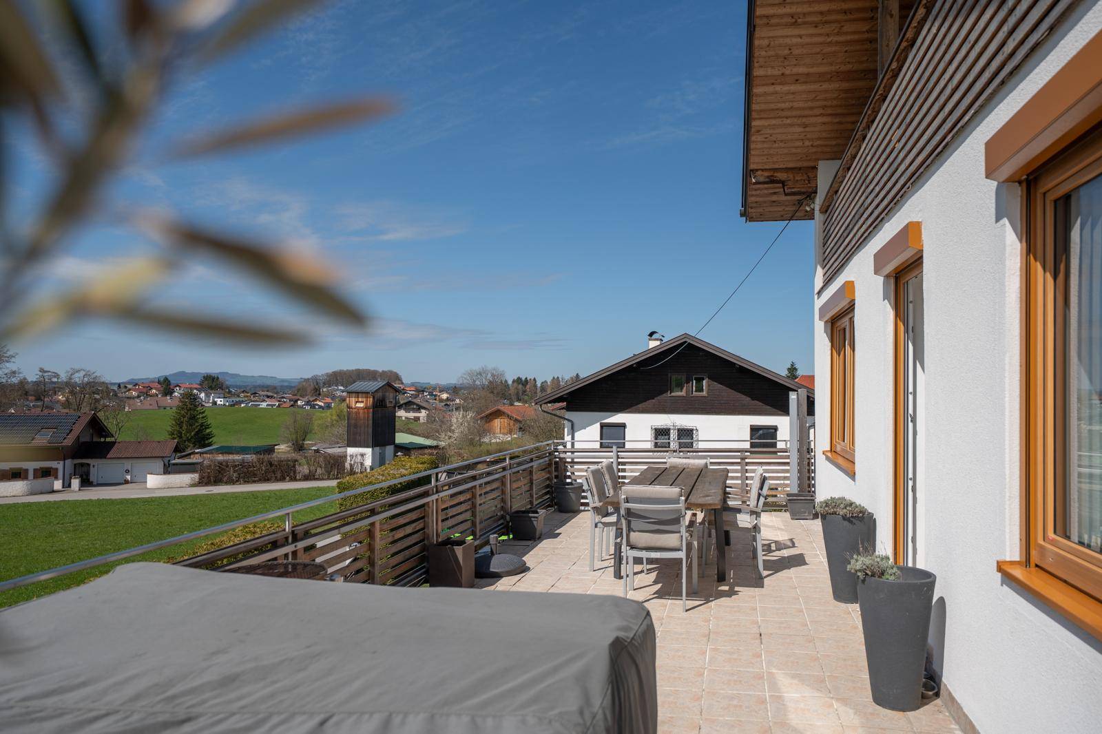 Große Sonnenterrasse mit Esstisch und Stühlen, umgeben von Pflanzen und mit weitem Blick ins Grüne.