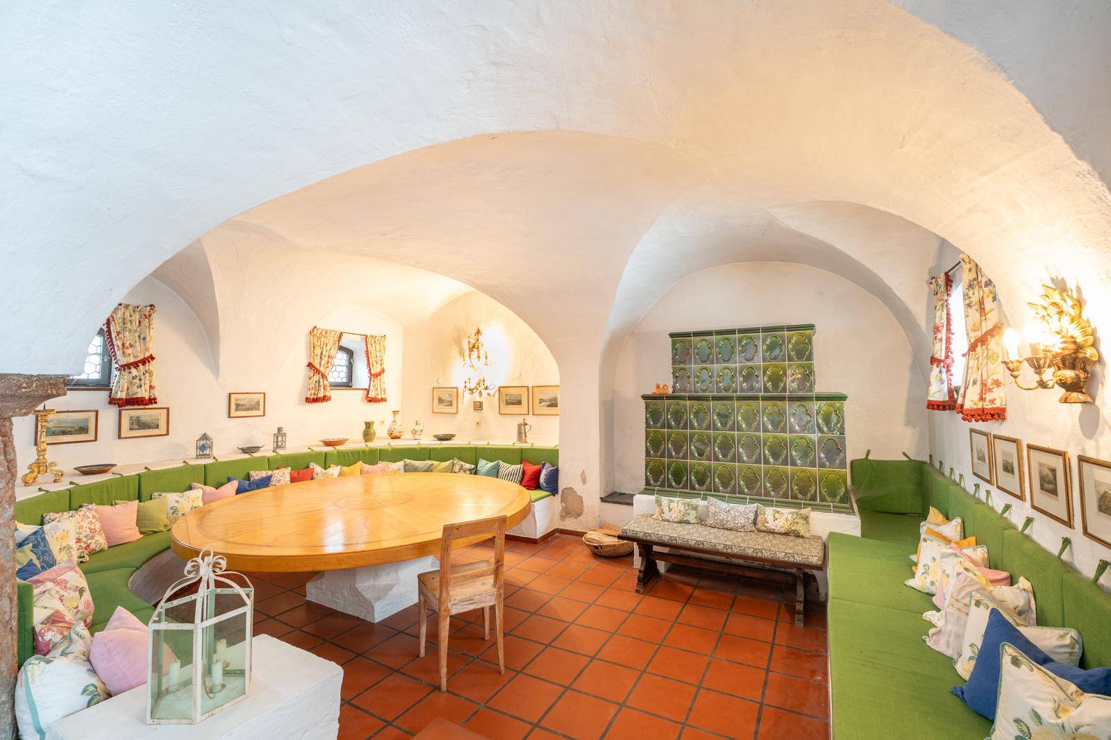 Geräumiger Essbereich mit traditionellem Kachelofen, Gewölbedecke und rustikalem Holztisch.
