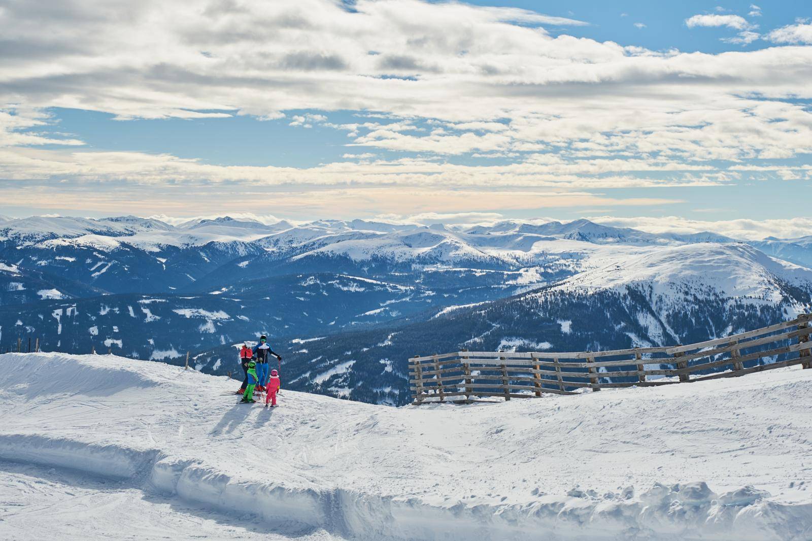 Skifahrer auf einer verschneiten Piste mit weitem Blick über eine beeindruckende Berglandschaft.