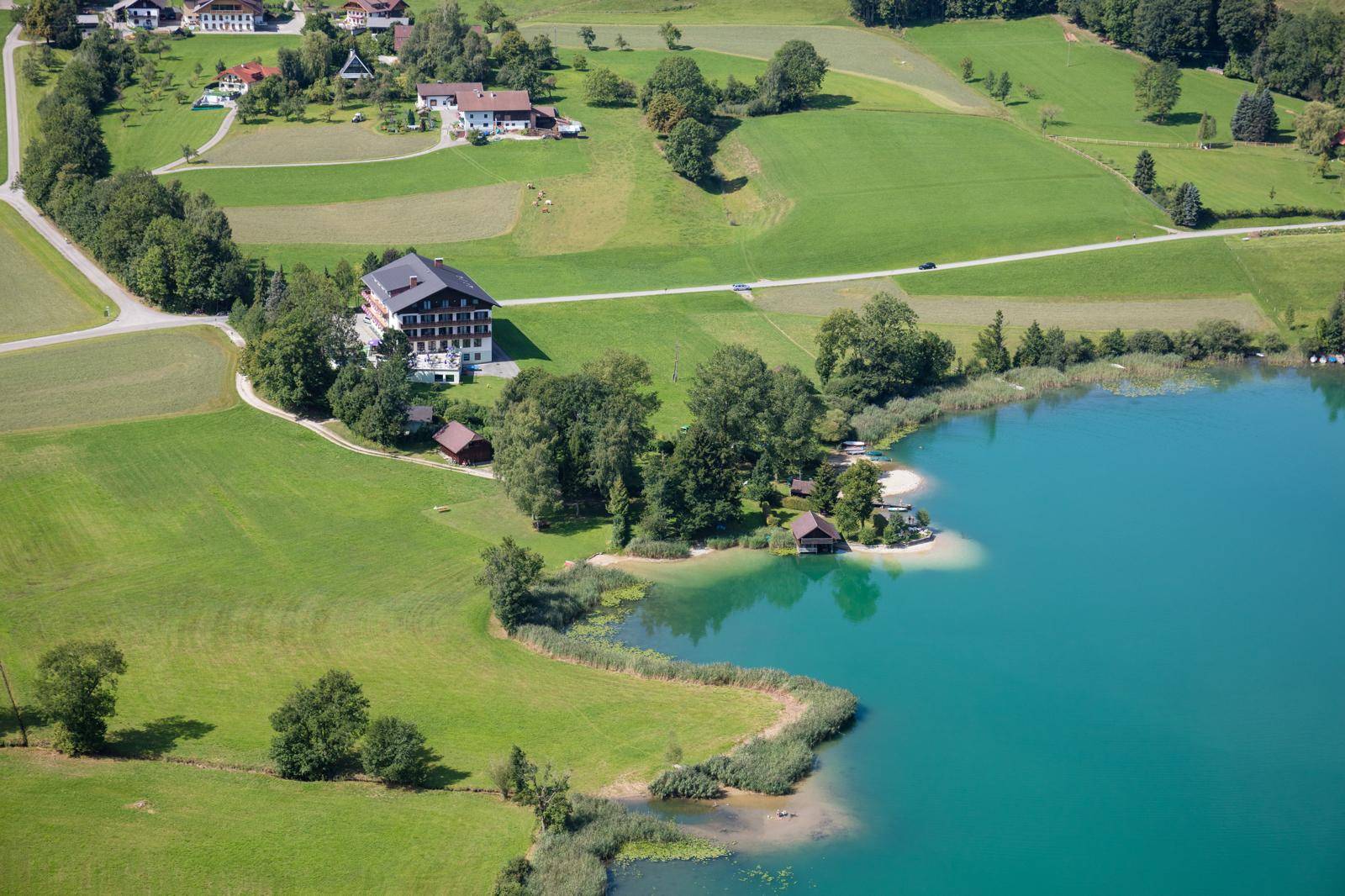Weitläufige Luftaufnahme des Gebäudes am See, umgeben von Feldern und kleinen Häusern.