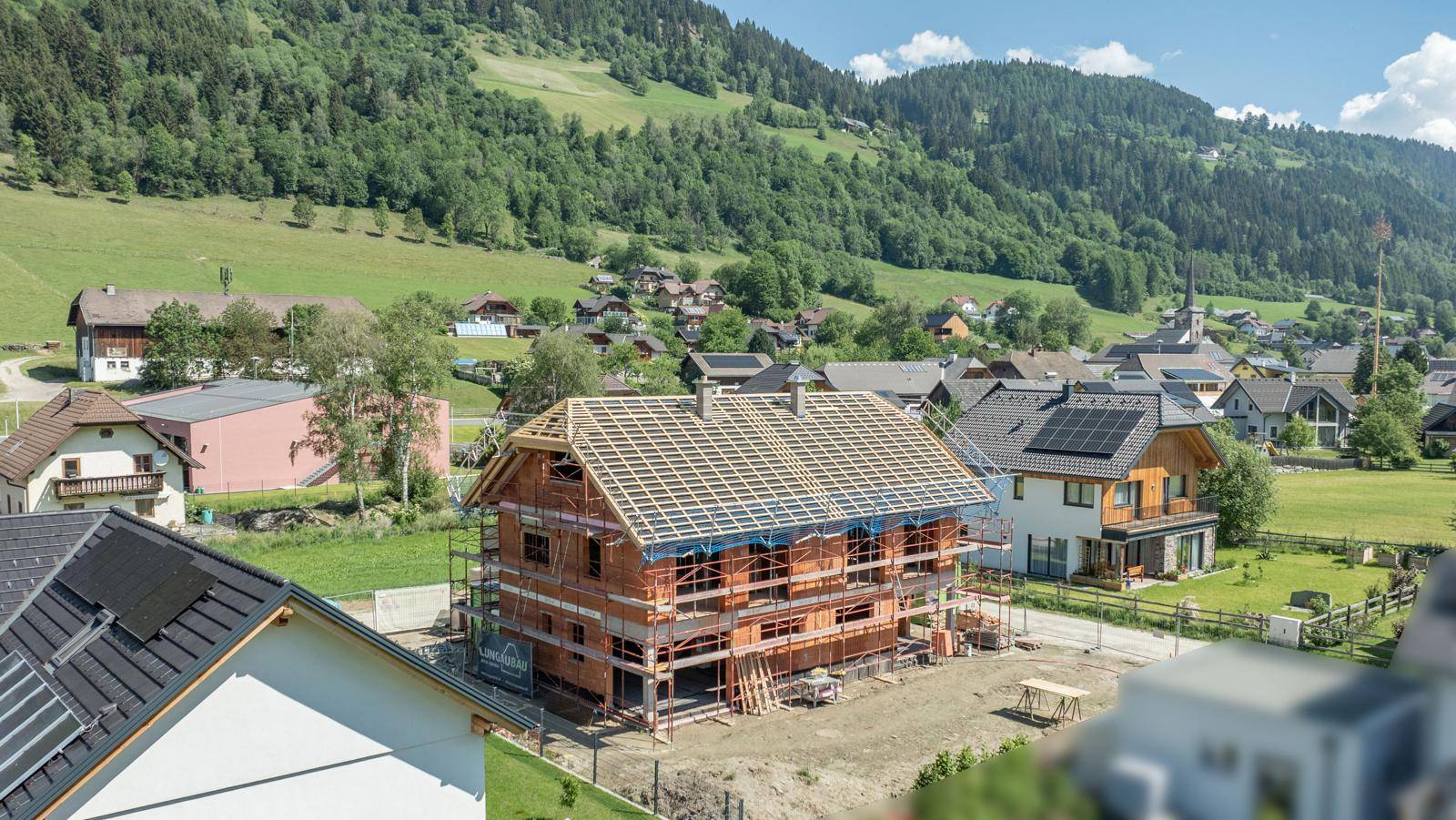 Baustelle eines Einfamilienhauses im Rohbau mit Dachstuhl und Blick auf ein Dorf.