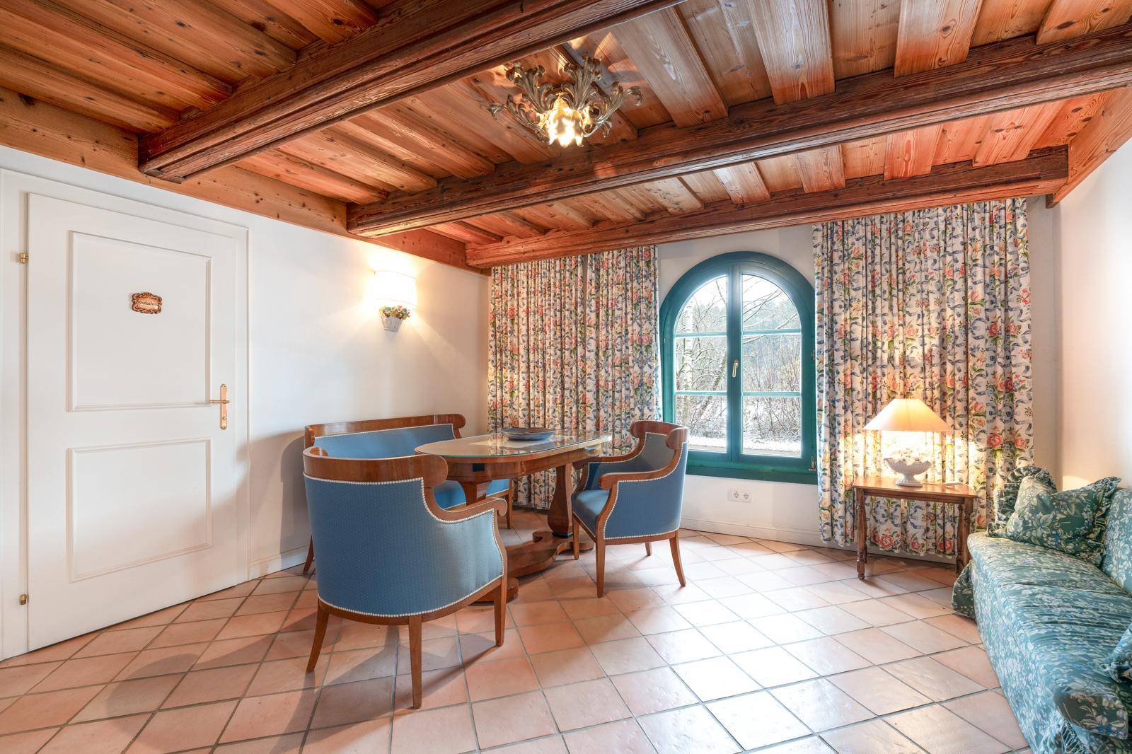 Kleiner Wohnbereich mit Holzbalkendecke, Fliesenboden und traditionellen blauen Sesseln.