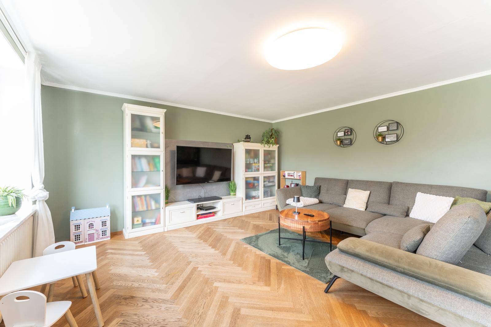 Gemütliches Wohnzimmer mit grün gestrichenen Wänden, Fischgrätparkett und großem Sofa für entspannte Stunden.