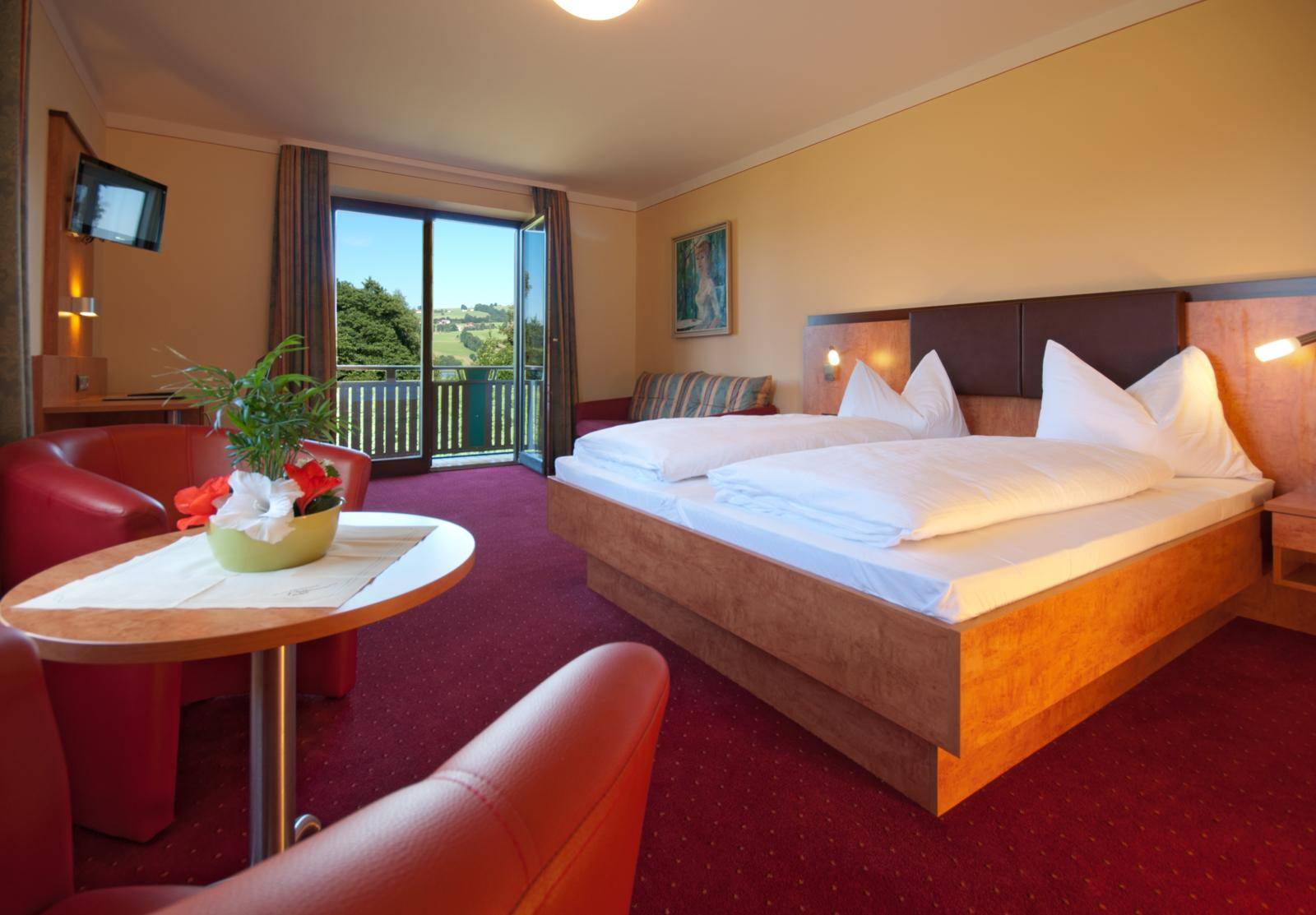 Komfortables Schlafzimmer mit rotem Teppich, Sitzgelegenheiten und Balkonzugang mit grüner Aussicht.