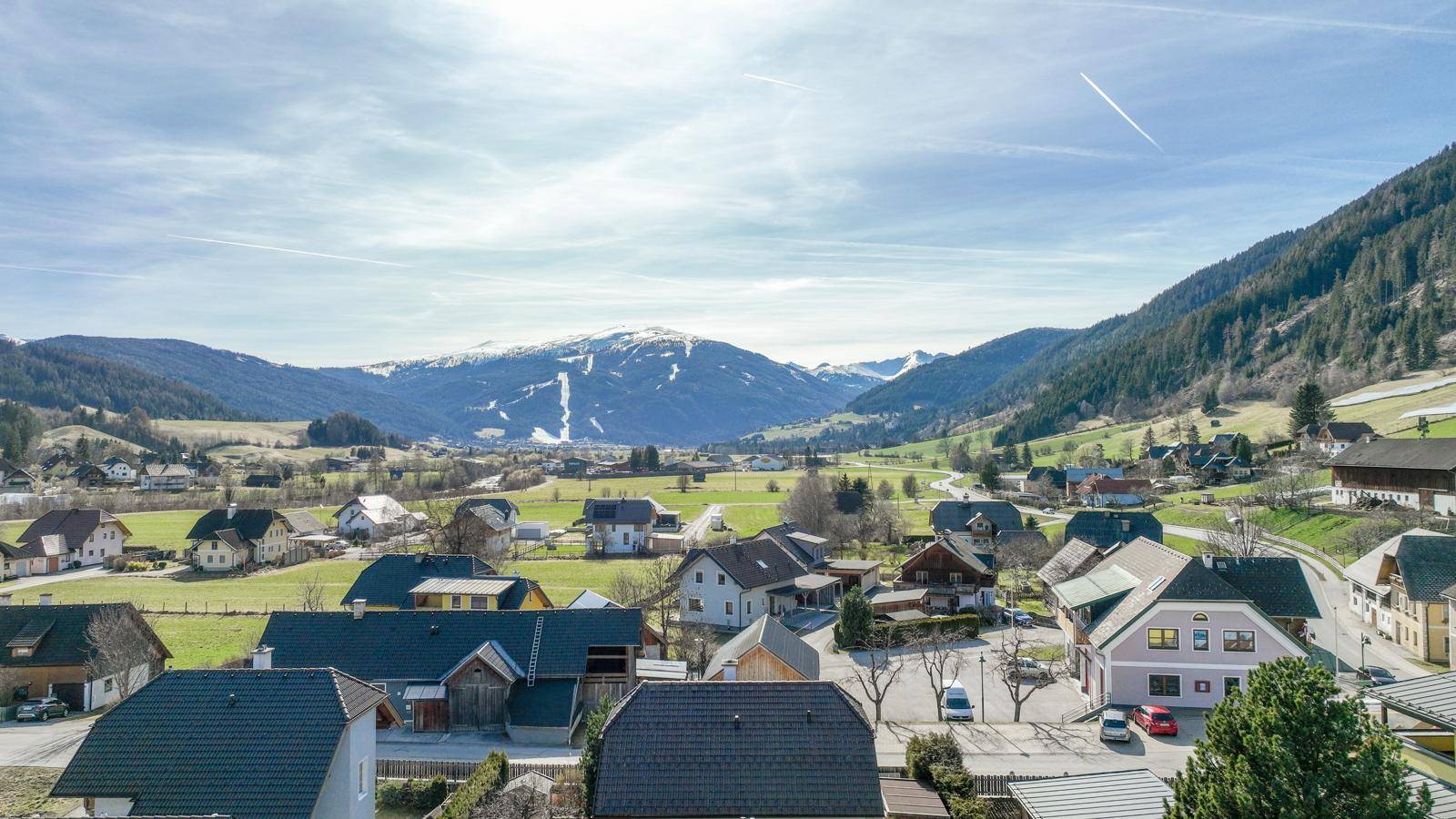 Weitläufige Landschaft mit ländlicher Bebauung und schneebedeckten Bergen im Hintergrund.