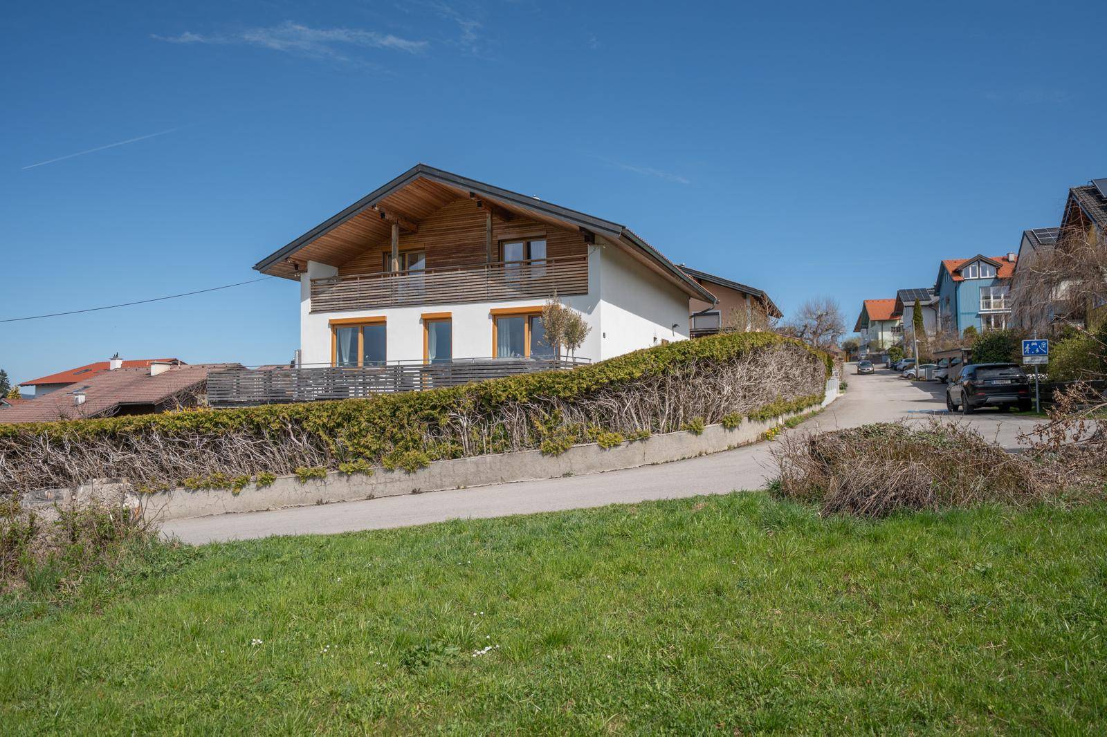 Einfamilienhaus mit moderner Architektur und gepflegter Hecke entlang der Straße in einer Wohnsiedlung.