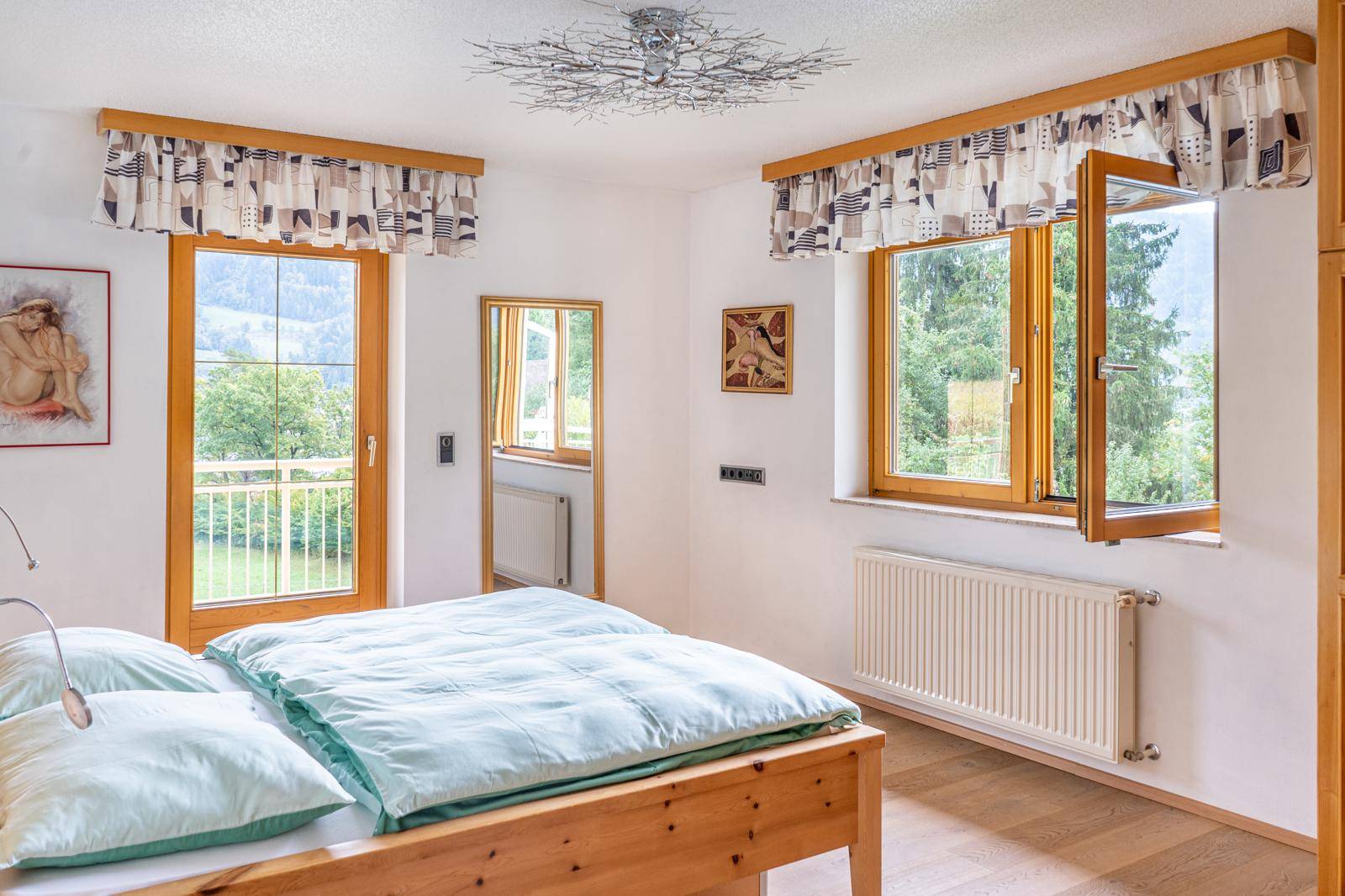 Helles Schlafzimmer mit Holzbett, großen Fenstern und direktem Zugang zu einem Balkon.