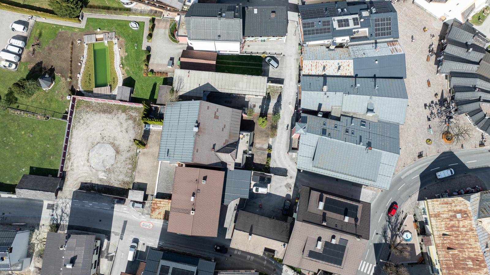 Vogelperspektive eines Dorfes mit zahlreichen Dächern, Straßen und einigen Grünflächen, Solaranlagen sichtbar.