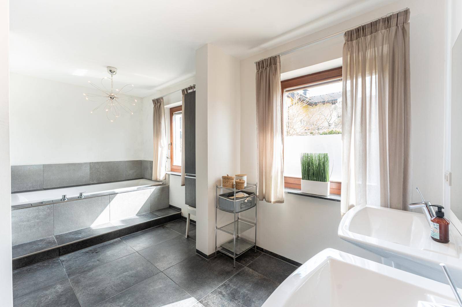 Geräumiges Badezimmer mit zwei Waschbecken, großer Badewanne und viel Tageslicht durch die Fenster.
