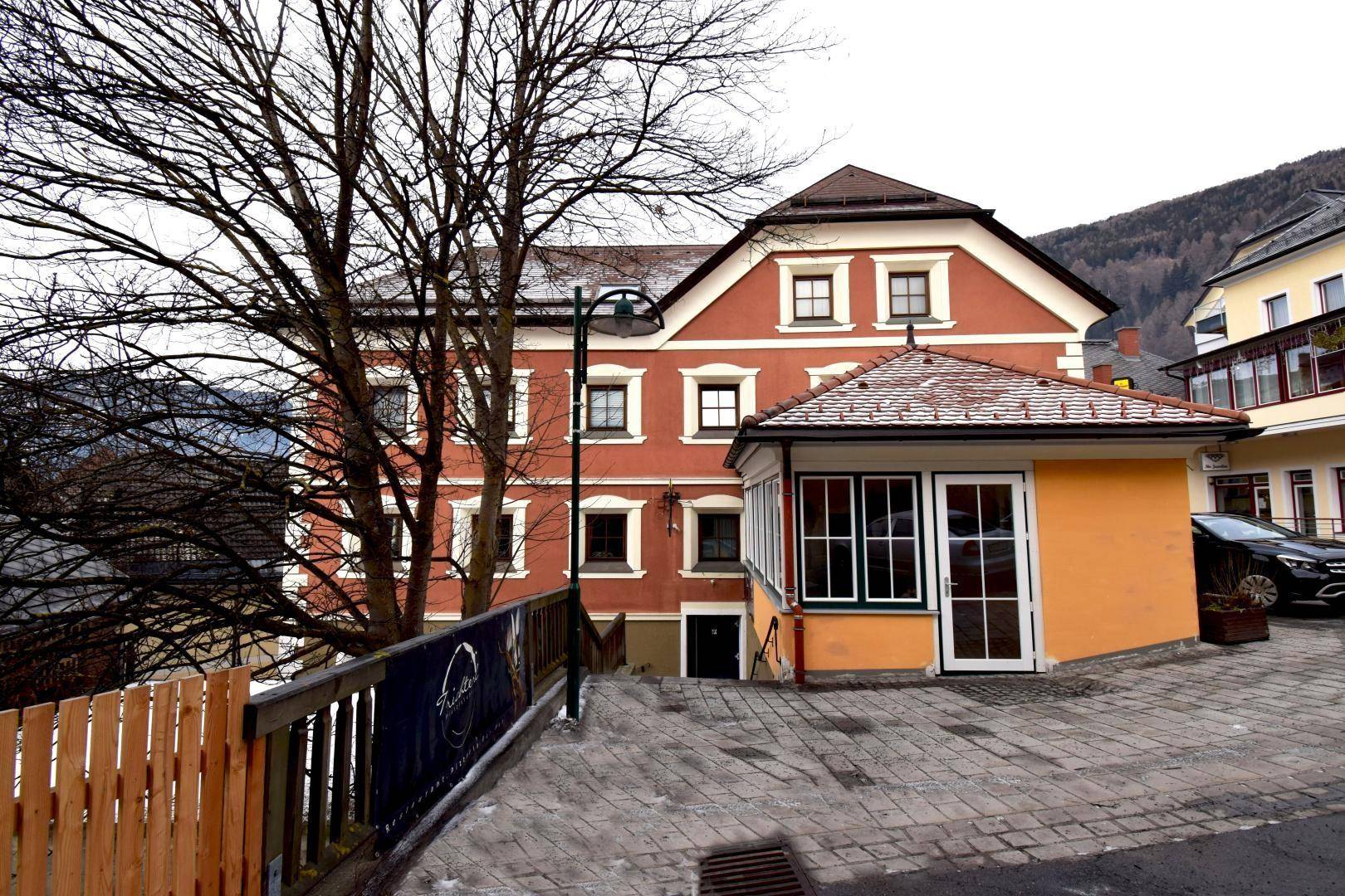 Traditionelles Gebäude mit roter Fassade und weiß abgesetzten Fenstern in einer bergigen Umgebung.