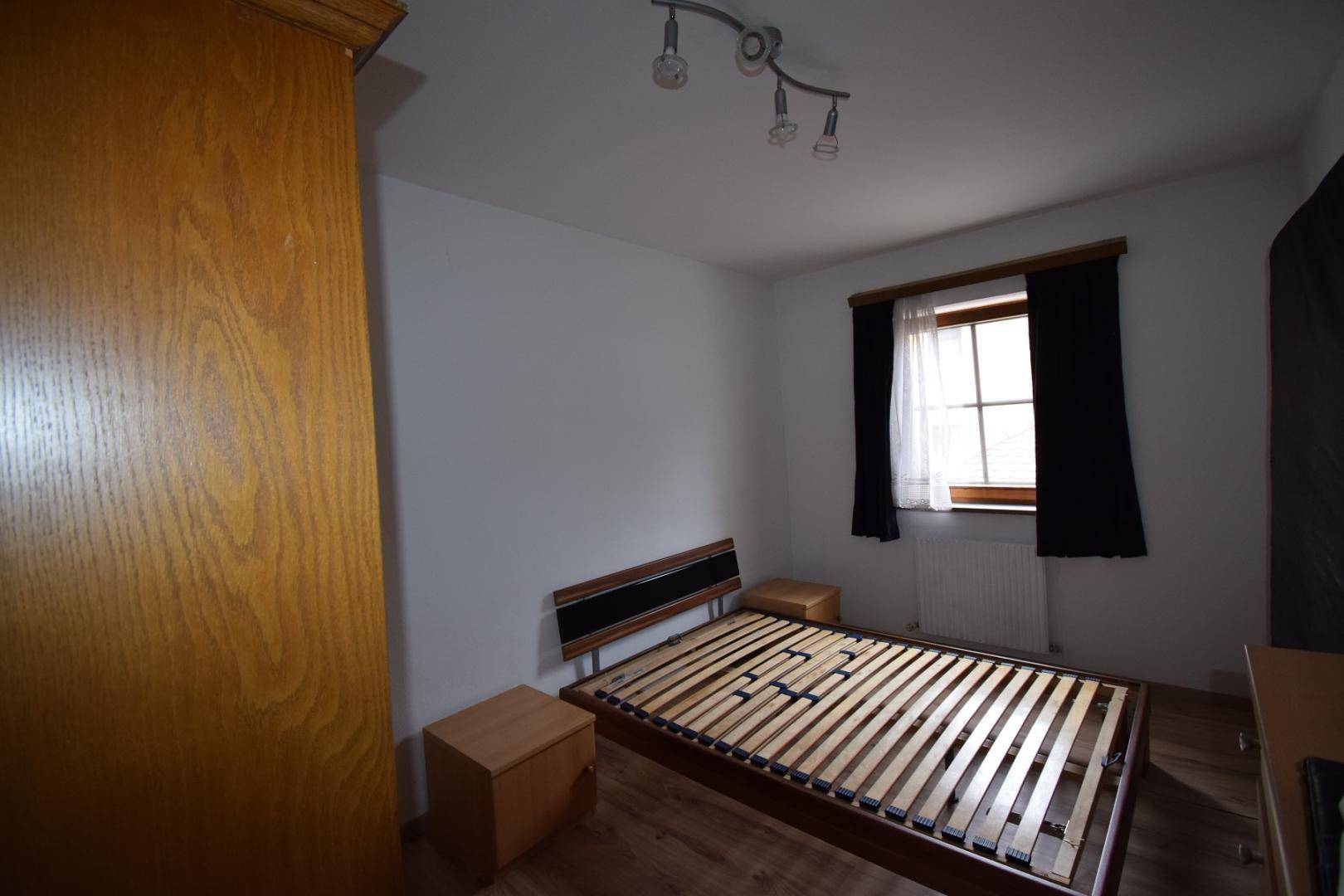 Schlafzimmer mit Holzbettrahmen, Nachttischen und einem Kleiderschrank aus hellem Holz.