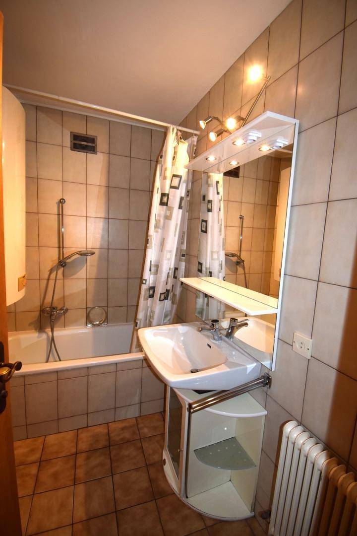 Gefliestes Badezimmer mit Badewanne, Duschvorhang, Waschbecken und Spiegelschrank.