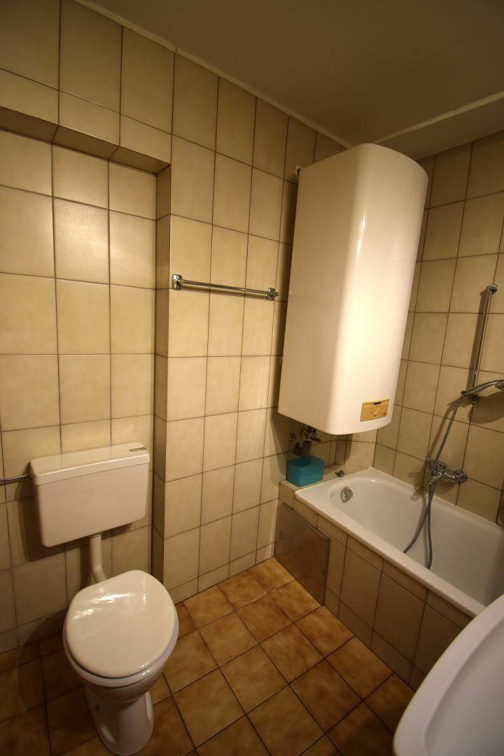 Badezimmer mit beigefarbenen Fliesen, Toilette und Badewanne mit Warmwasserboiler.