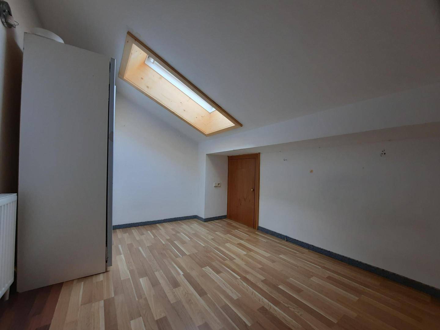 Geräumiger Dachgeschossraum mit Holzboden, schräger Decke und einem hellen Dachfenster.