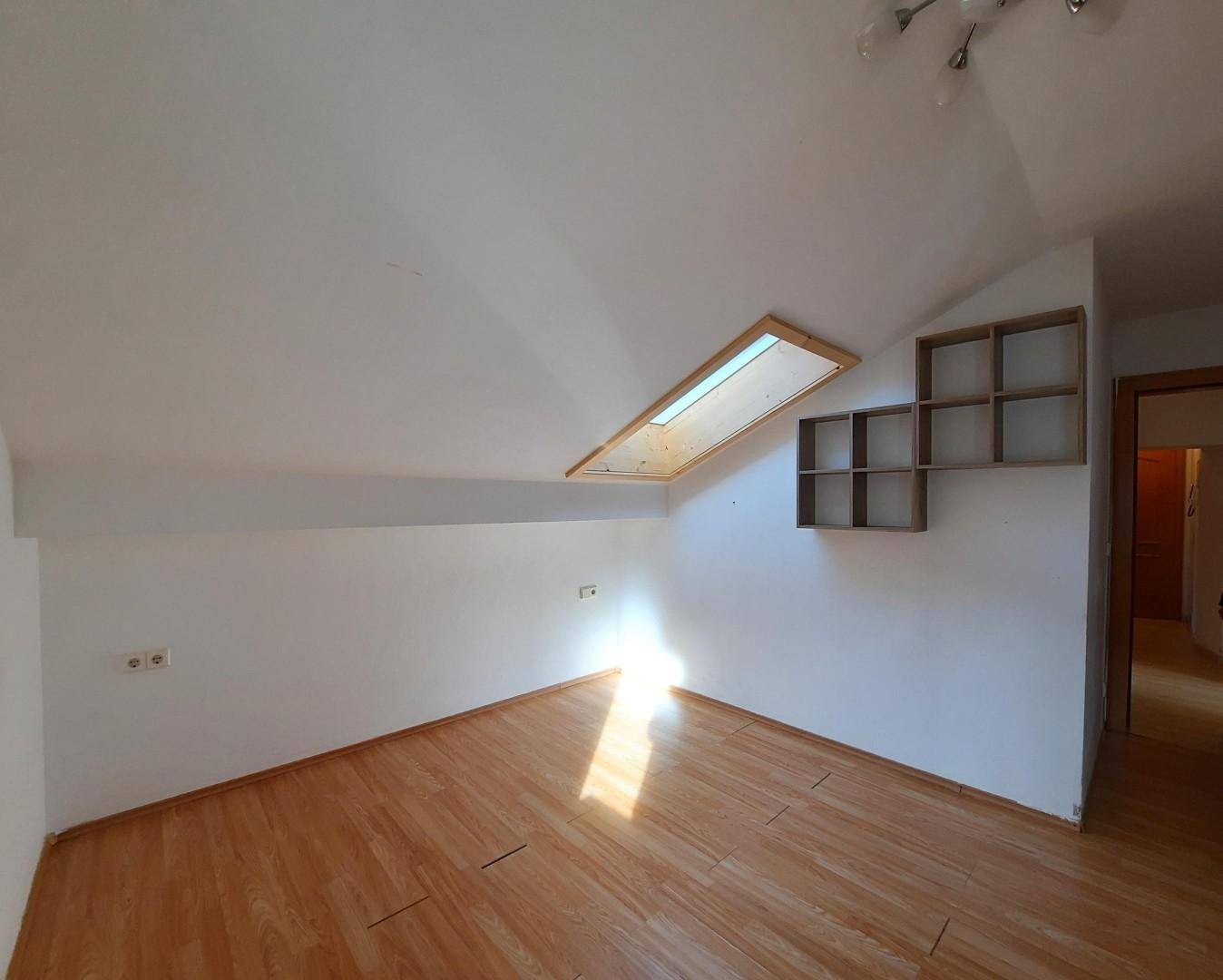 Heller Dachgeschossraum mit Laminatboden, schräger Decke und einem großen Dachfenster.