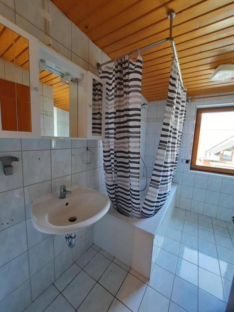 Funktionales Badezimmer mit Badewanne, Duschvorhang, Waschbecken und Holzdecke im Dachgeschoss.