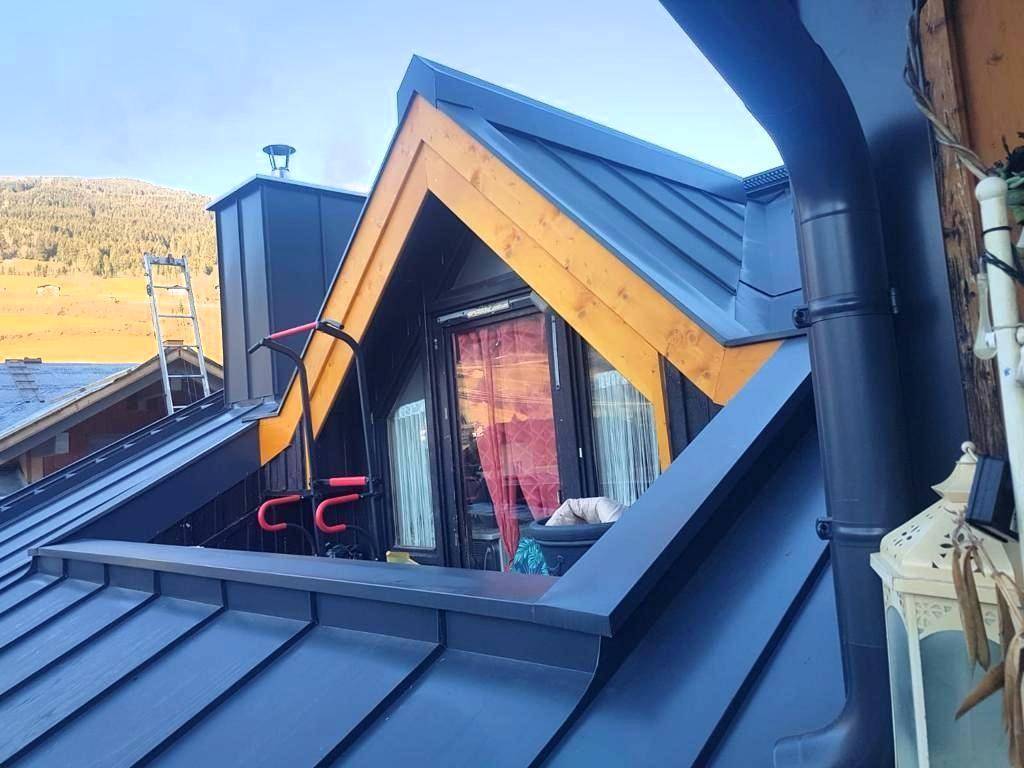Moderne Dachkonstruktion mit dunklen Metallpaneelen und hölzernen Giebelverkleidungen.