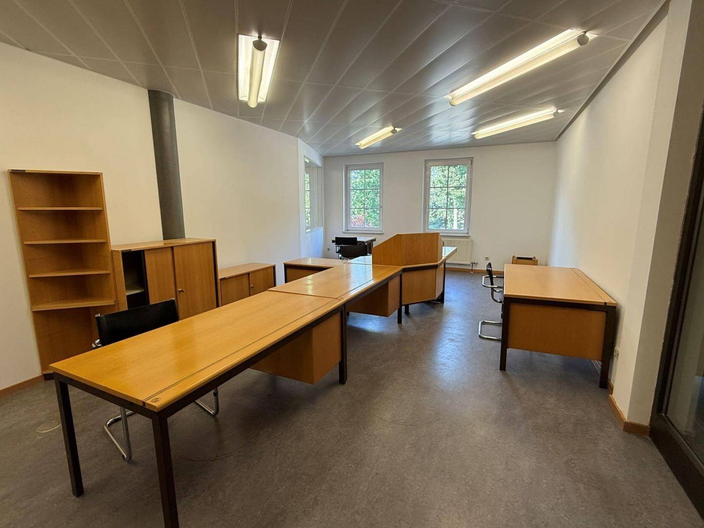 Geräumiges Büro mit mehreren Holzschreibtischen, Regalen und Fenstern mit Blick ins Grüne.