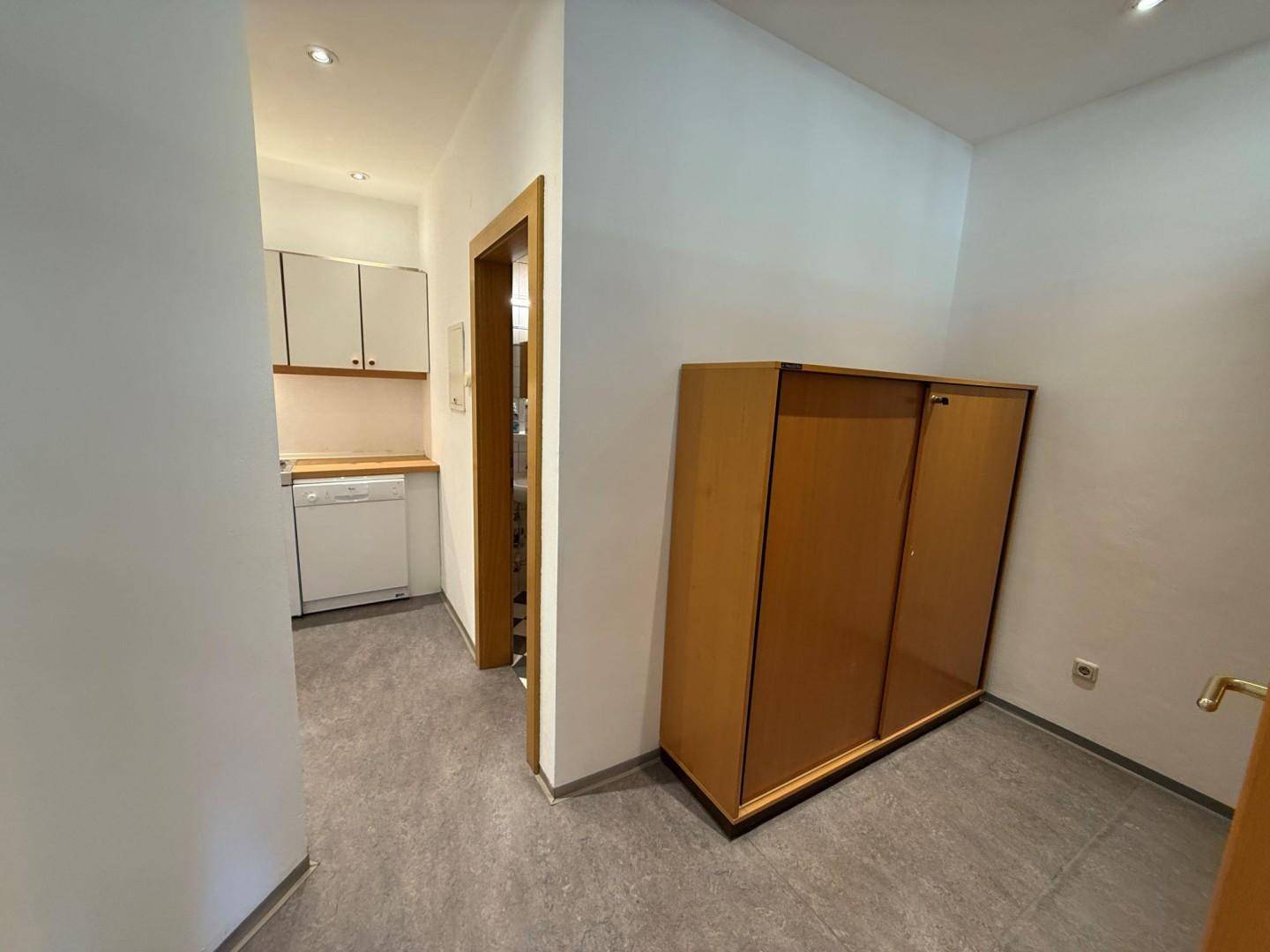 Kleiner Flur führt zu einer kompakten Küchenzeile mit weißen Schränken und einem Schrank im Vordergrund.