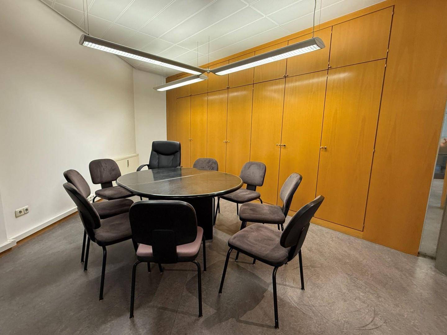 Konferenzraum mit einem runden Tisch, mehreren Stühlen und einer Wand aus Holzschränken.
