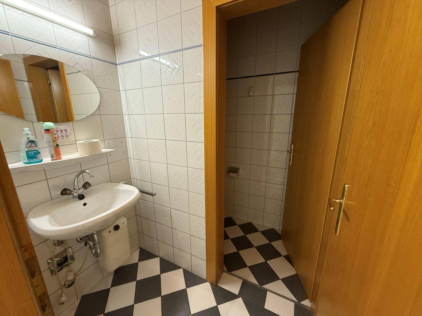 Badezimmer mit Waschbecken, Spiegel und schwarz-weiß karierten Fliesen auf dem Boden.