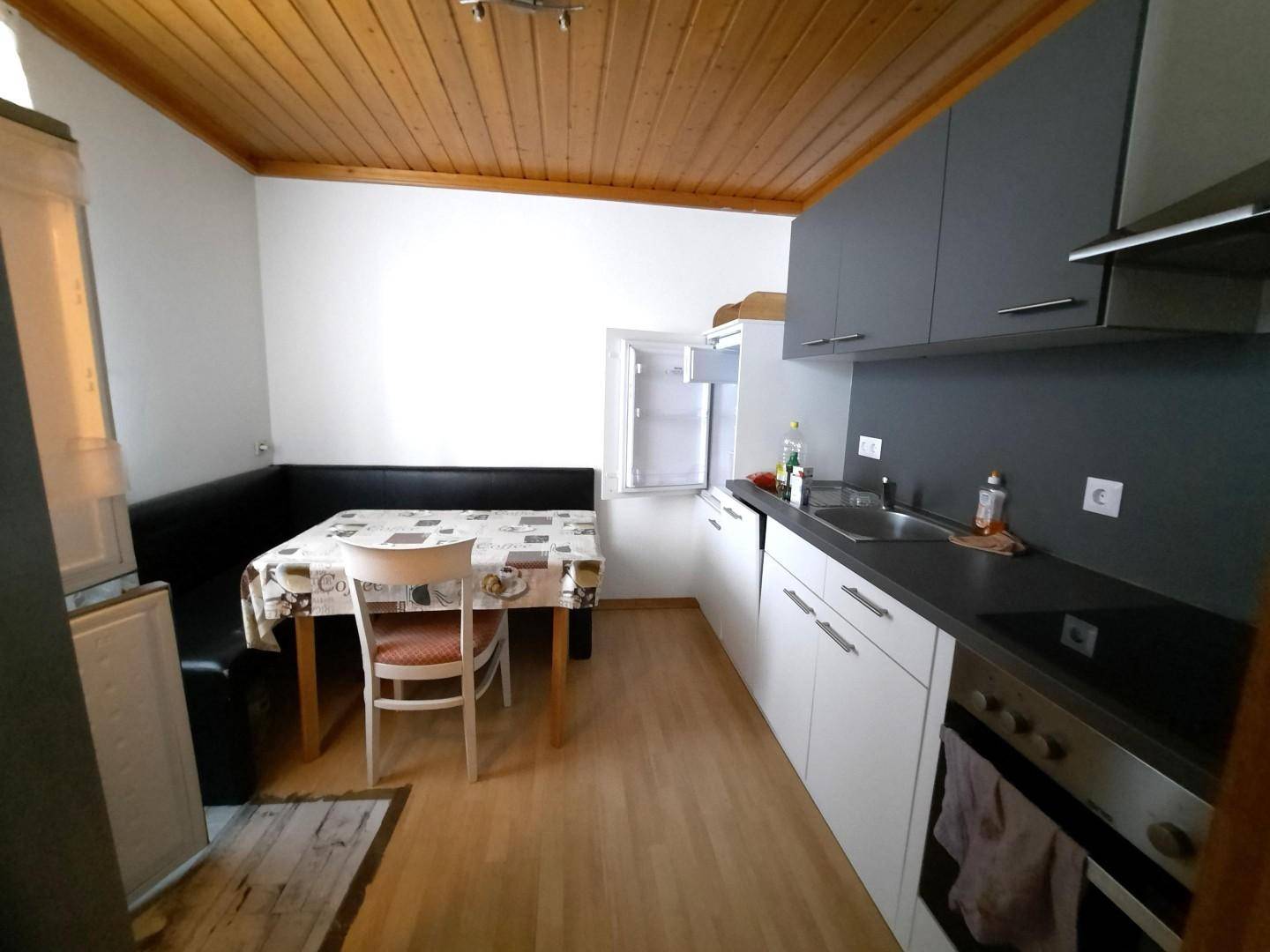 Küche mit Essbereich, Holzbalkendecke und modernen grauen und weißen Schränken.