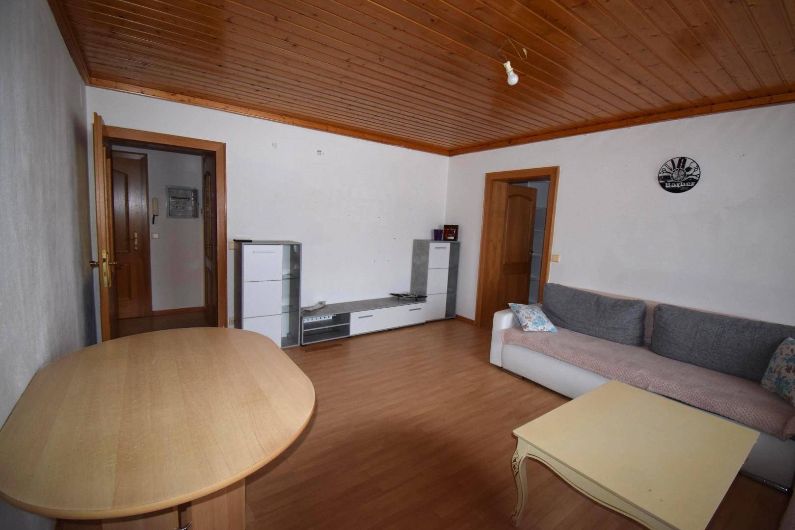 Gemütliches Wohnzimmer mit Holzbalkendecke, Laminatboden und einfacher Einrichtung.