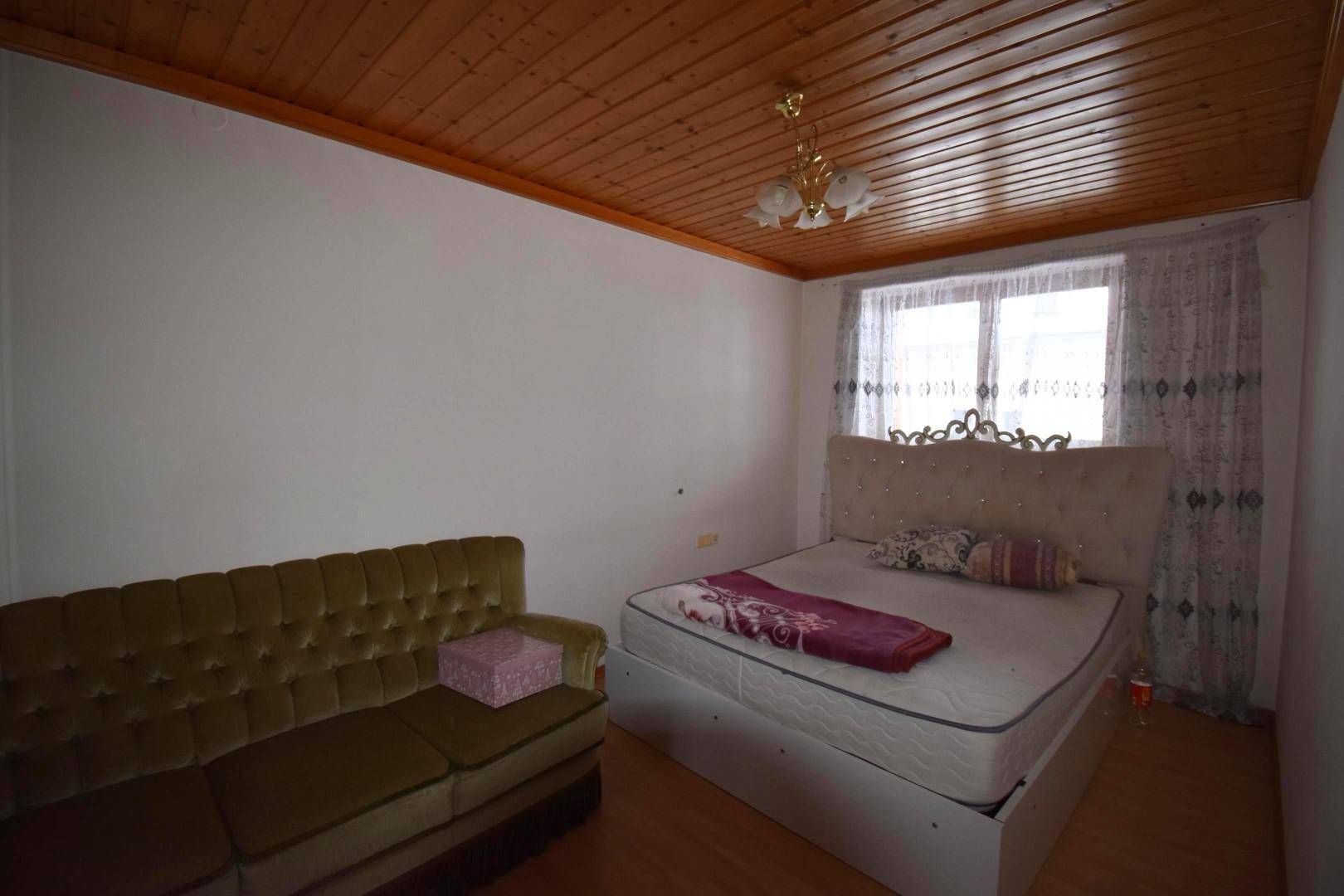 Schlafzimmer mit Holzbalkendecke, Doppelbett und einem Sofa, hell durch das Fenster.