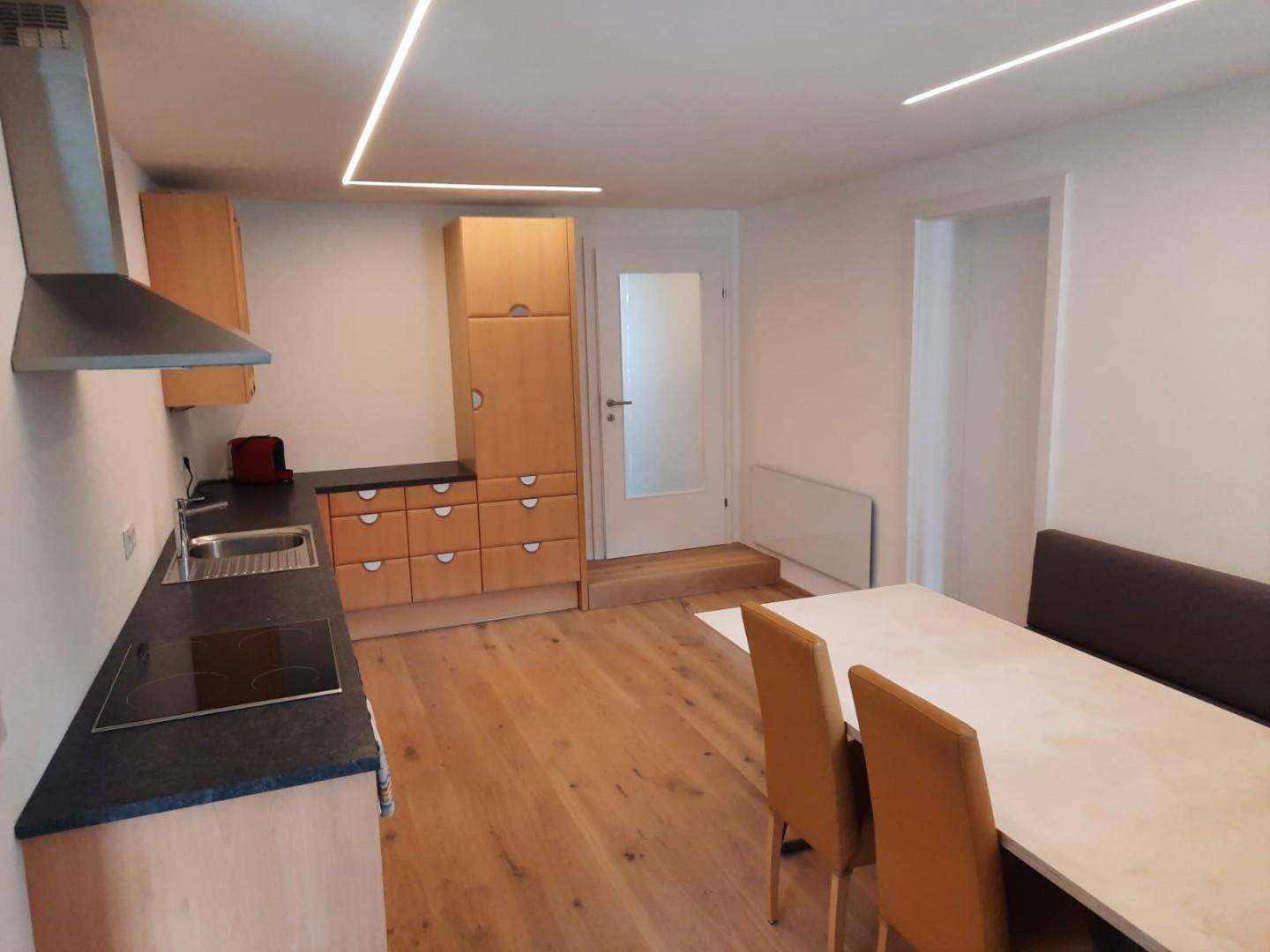 Moderne Küche mit hellen Holzschränken, dunkler Arbeitsplatte und integriertem Essbereich.