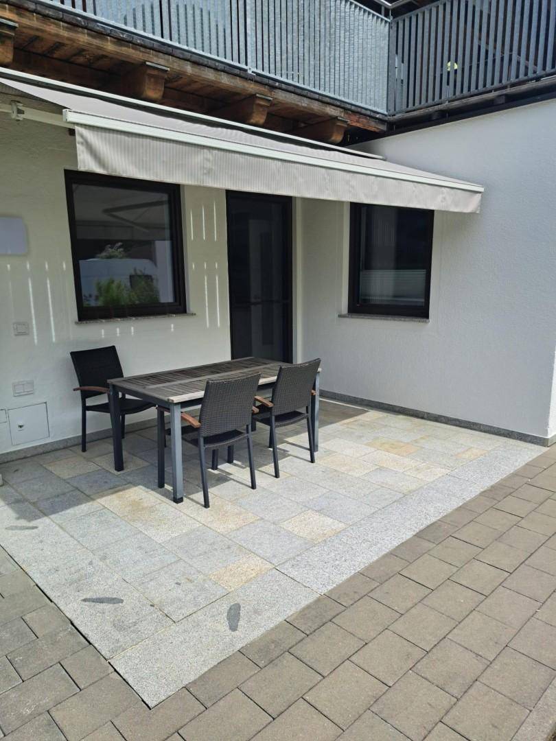 Sonniger Terrassenbereich mit Esstisch, Stühlen und einer ausfahrbaren Markise.
