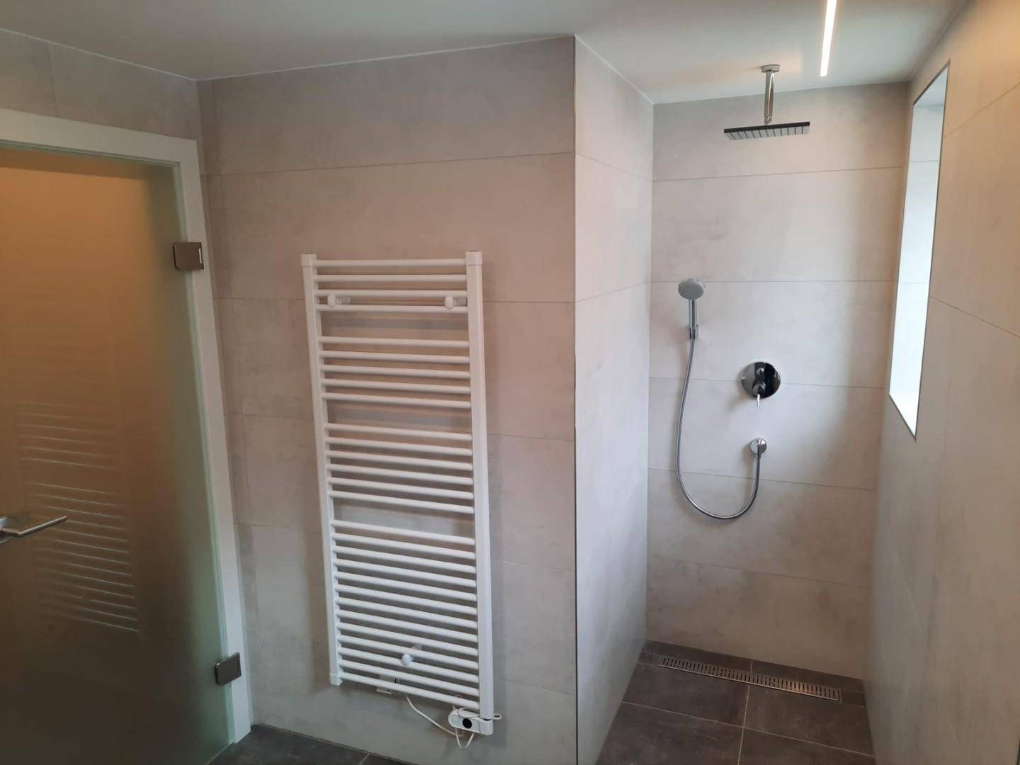 Modernes Badezimmer mit ebenerdiger Dusche, Regendusche und beheiztem Handtuchhalter.