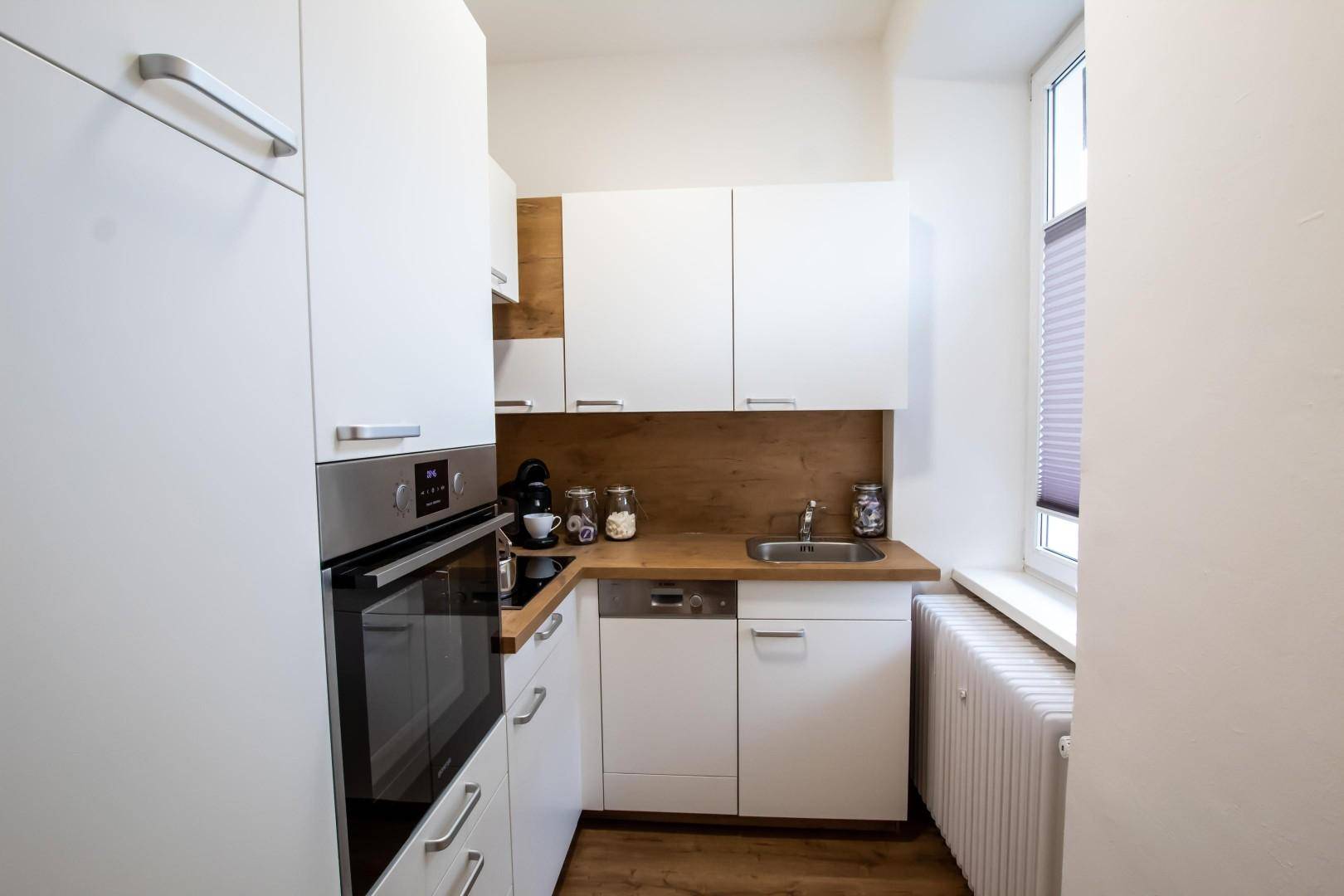 Kompakte, moderne Küche mit weißen Schränken, Einbauofen und Fenster.
