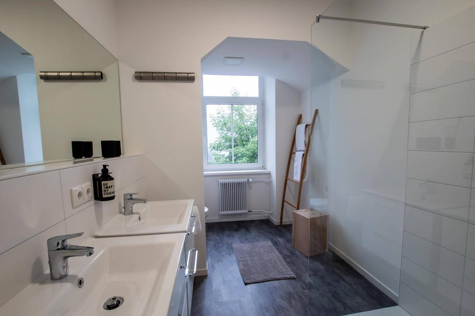 Modernes Badezimmer mit Doppelwaschbecken, begehbarer Dusche und Fenster.