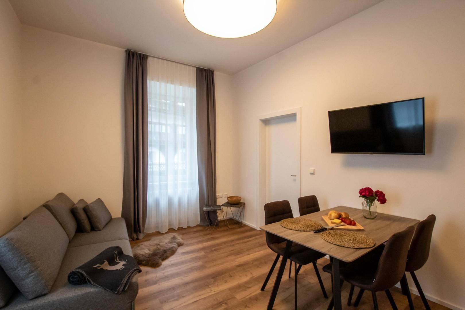 Heller Wohn-Essbereich mit Sofa, Esstisch und an der Wand montiertem Fernseher.