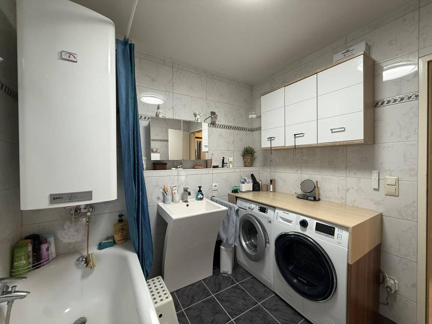 Funktionales Badezimmer mit Badewanne, Waschbecken und Waschmaschine, hell gefliest.