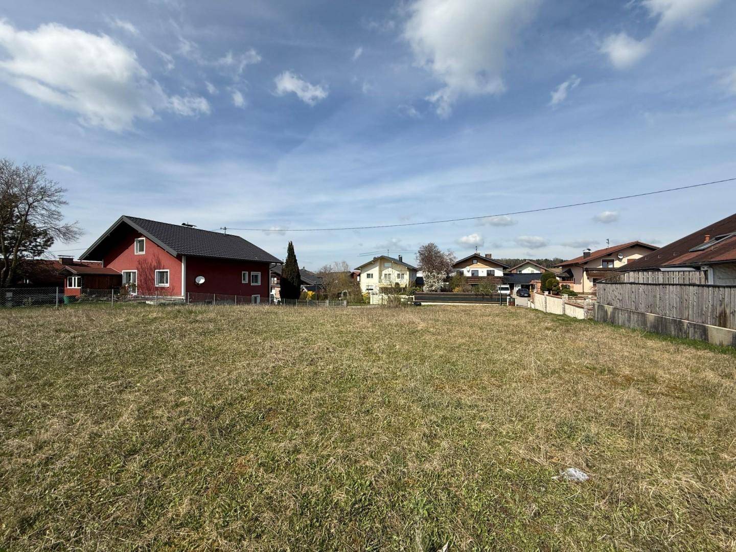 Weitläufiges Grundstück mit Grasfläche und angrenzenden Wohnhäusern unter bewölktem Himmel.