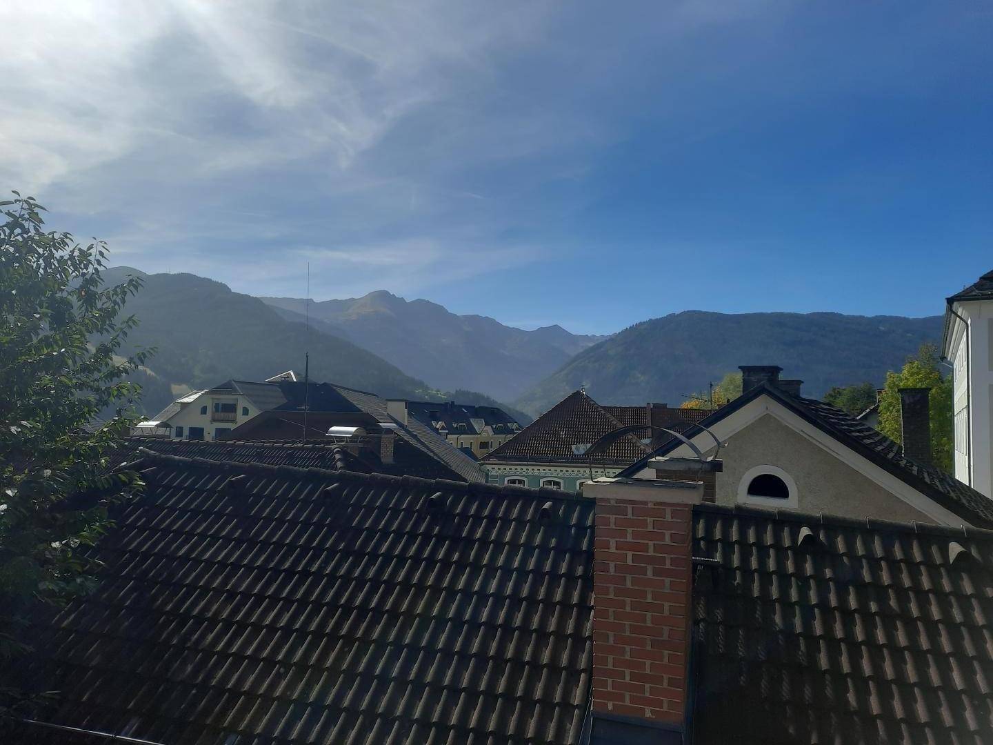 Weitblick über Dächer auf eine beeindruckende Berglandschaft unter blauem Himmel.