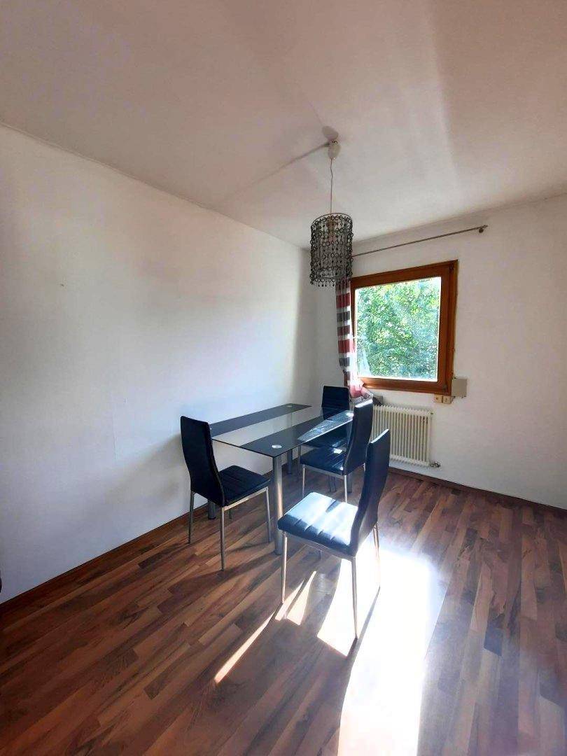 Essbereich mit modernem Glastisch, dunklen Stühlen und Holzboden, beleuchtet durch ein Fenster.