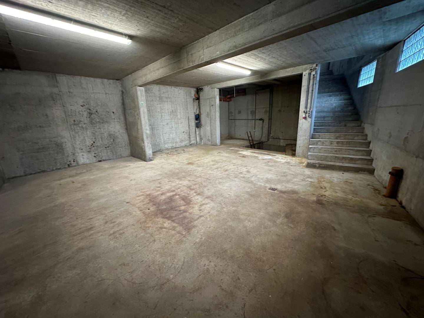 Großer, unfertiger Kellerraum mit Betonwänden und -boden sowie einer Treppe.