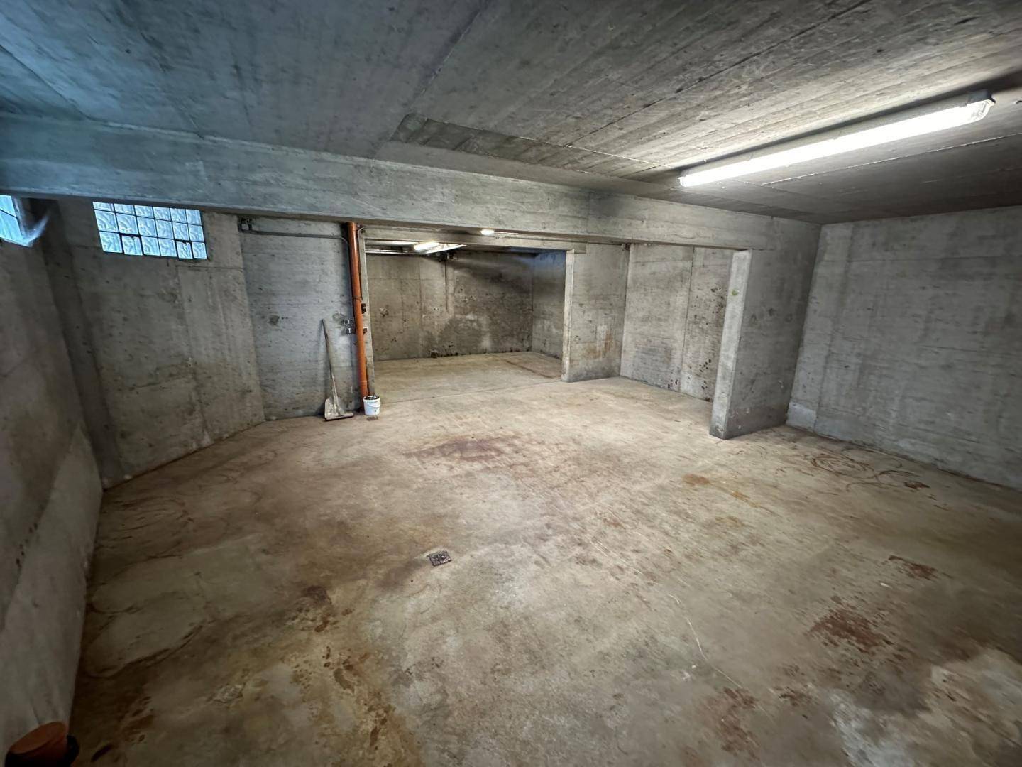 Weiterer Blick in den Kellerraum mit Betonwänden, Rohren und einem kleinen Fenster.