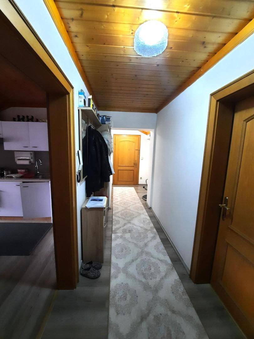 Heller Flur mit Holzdecke, Garderobe und einem Teppichläufer, der zu den angrenzenden Räumen führt.