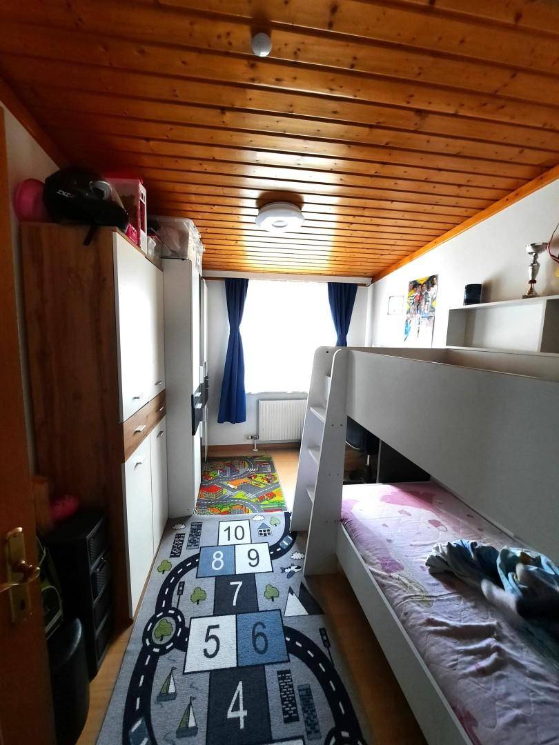 Kinderzimmer mit Etagenbett, Holzdecke und einem spielerischen Teppich, der zum Spielen einlädt.