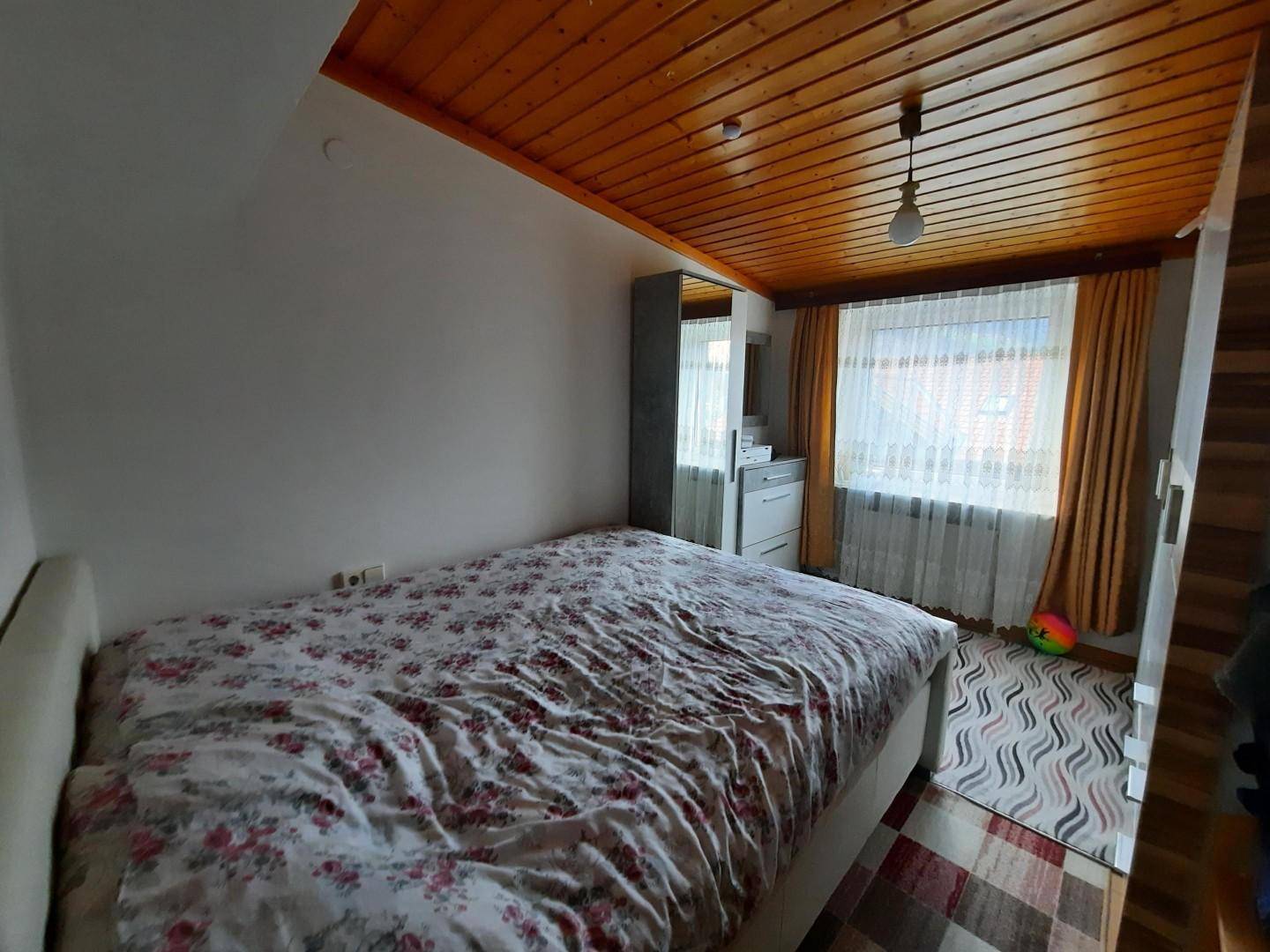 Schlafzimmer mit Einzelbett, Kleiderschrank und einer charmanten Holzdecke, die eine warme Atmosphäre schafft.