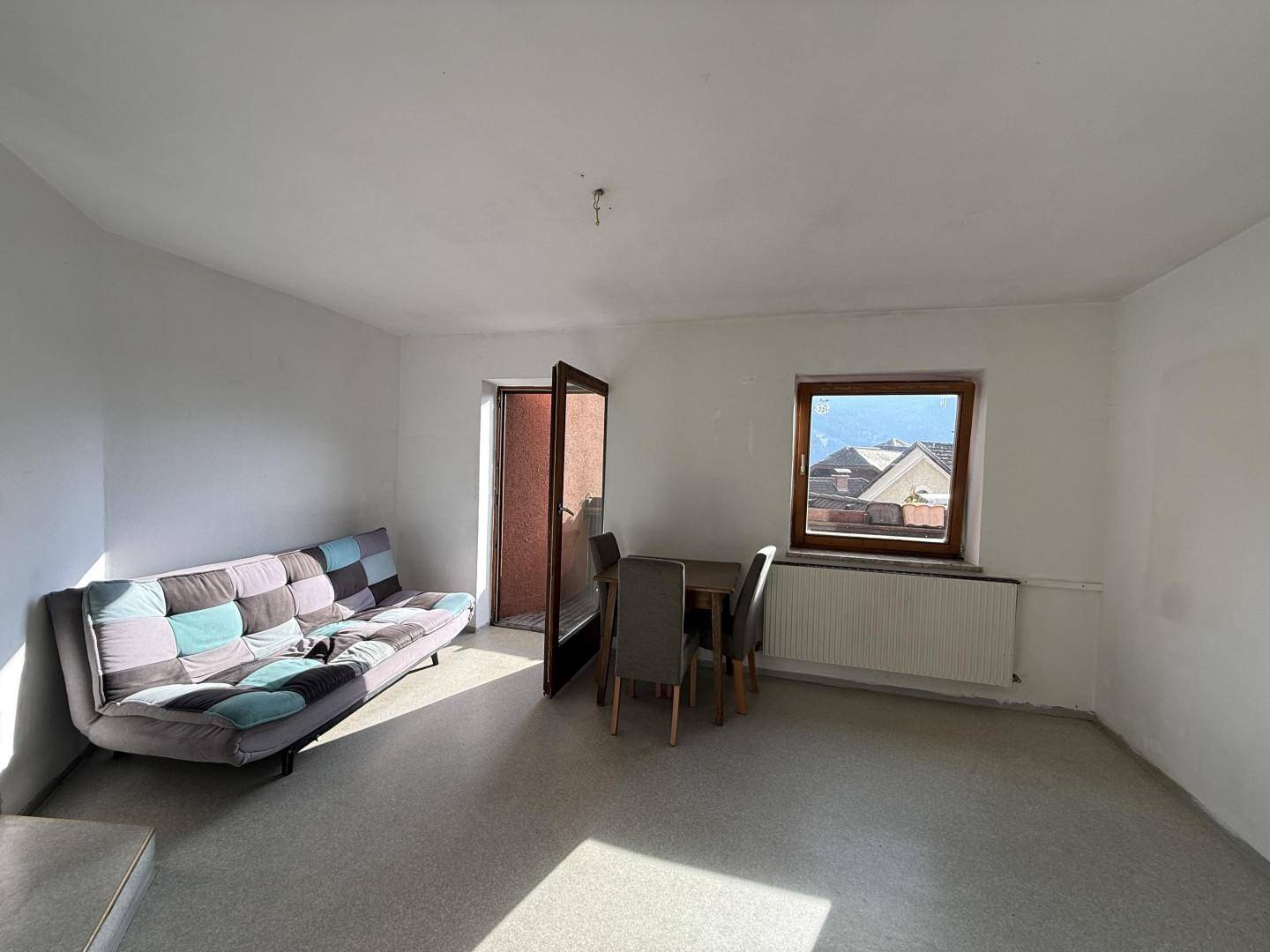 Helles Zimmer mit Sofa, kleinem Esstisch und Blick auf die Dächer der Umgebung.