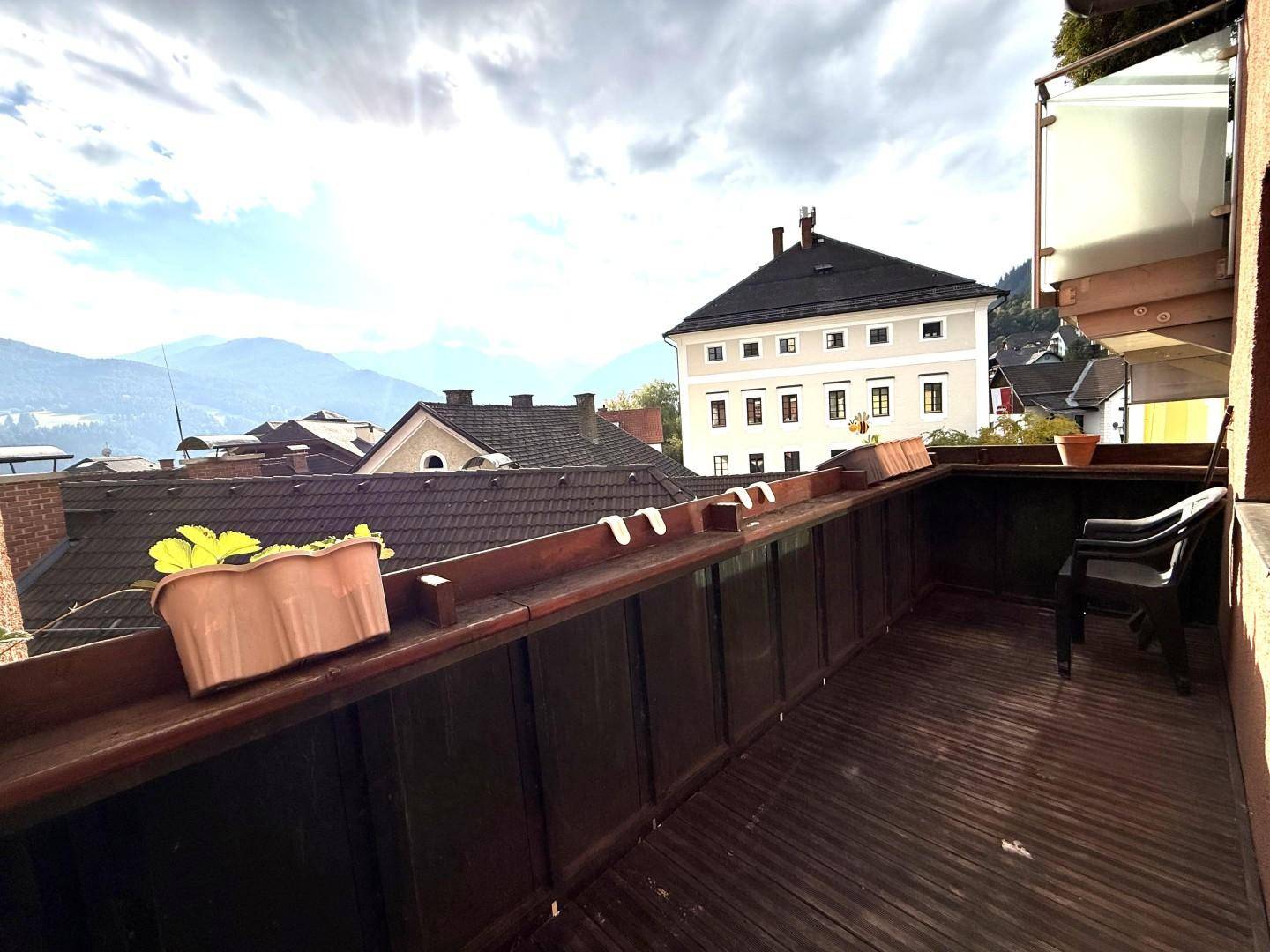 Balkon mit Holzboden, Geländer und Blick auf die umliegenden Häuser und Berge.