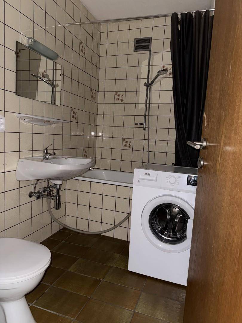 Badezimmer mit Badewanne, Dusche, WC und Waschmaschine, gefliest in Beige und Braun.