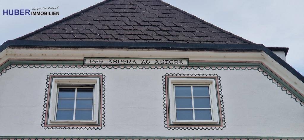 Dachbereich eines historischen Gebäudes mit zwei Fenstern und lateinischer Inschrift über dem Giebel.