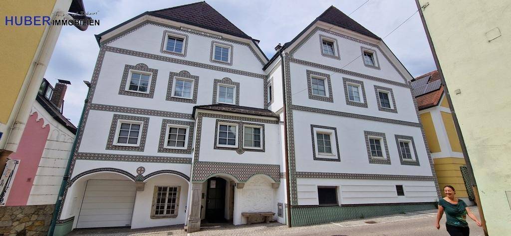 Historisches Gebäude mit weißer Fassade und dezenten Mustern in einer engen Gasse.