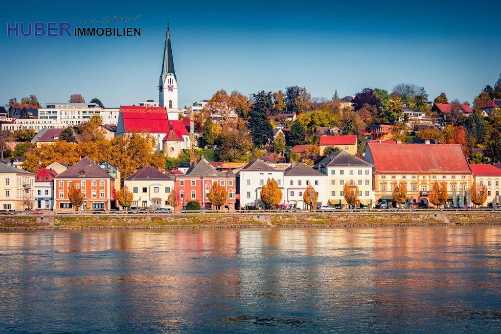 Panoramablick auf eine malerische Stadt am Flussufer mit historischer Architektur und Kirchturm.